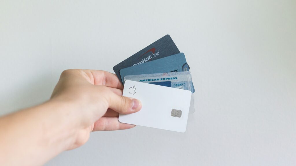 Hand holding multiple credit cards including Apple Card and American Express fanned out against a white background